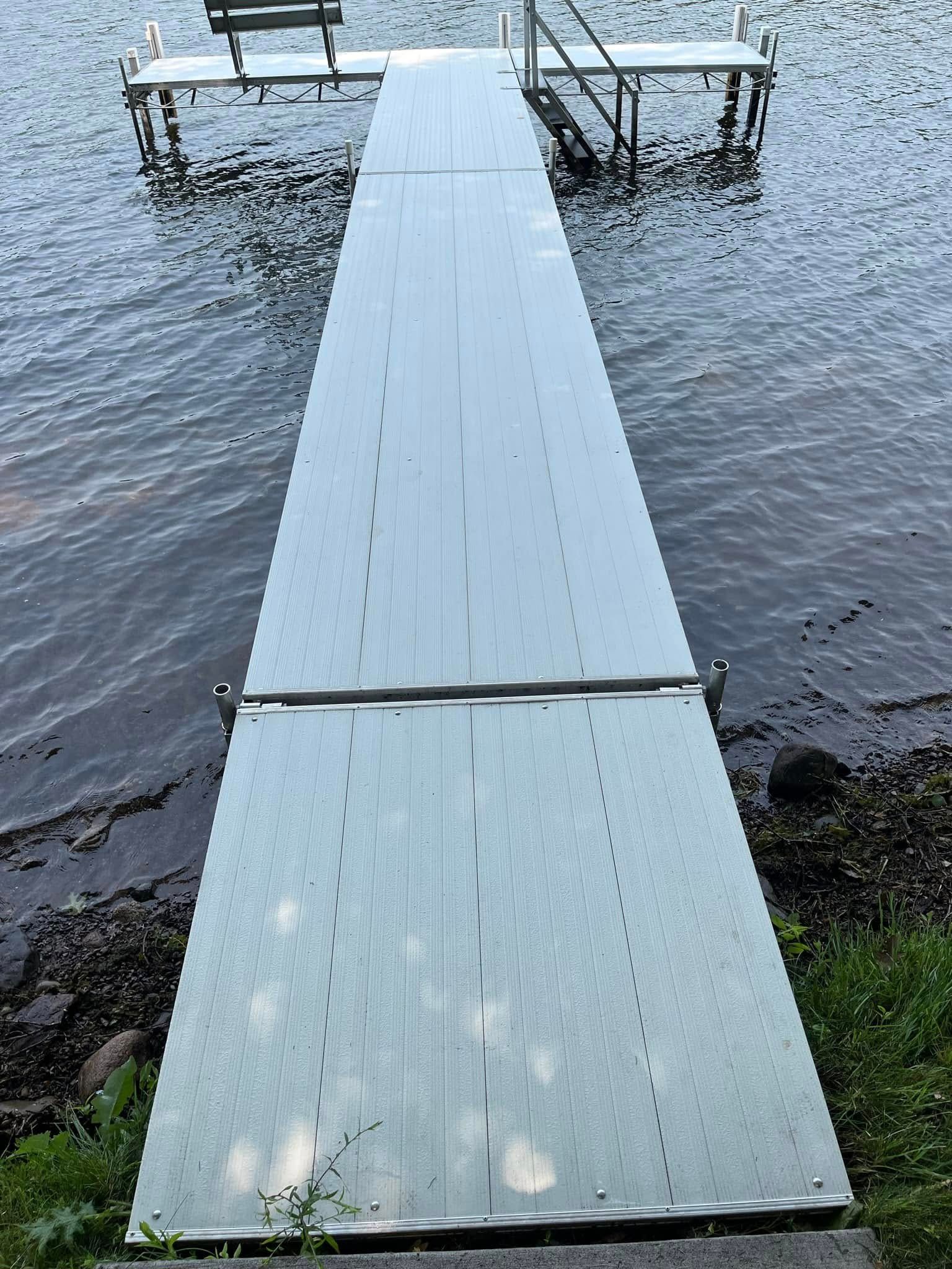 Narrow white dock leading over water to a small floating platform with railings