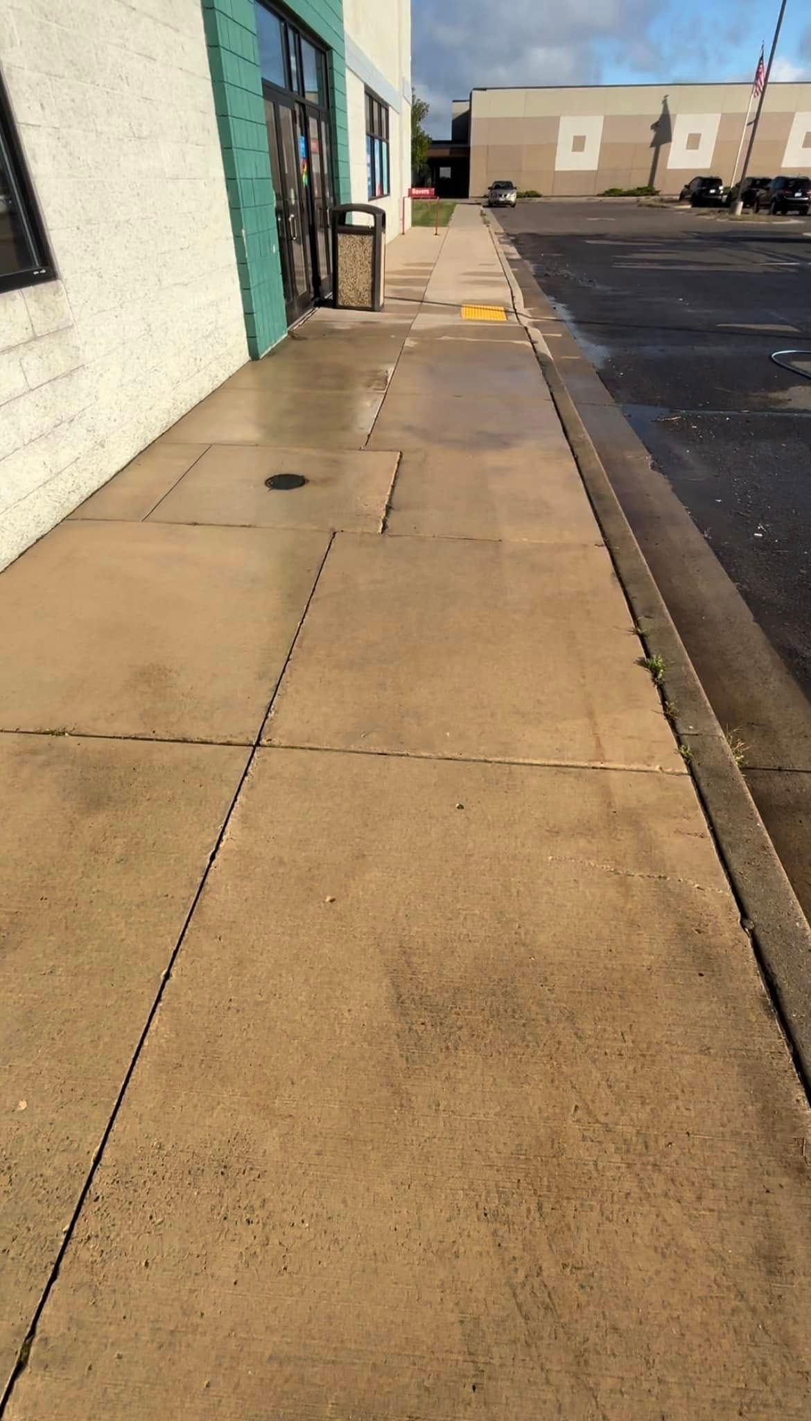 Empty sidewalk beside a building, with a street and parked cars along the curb.