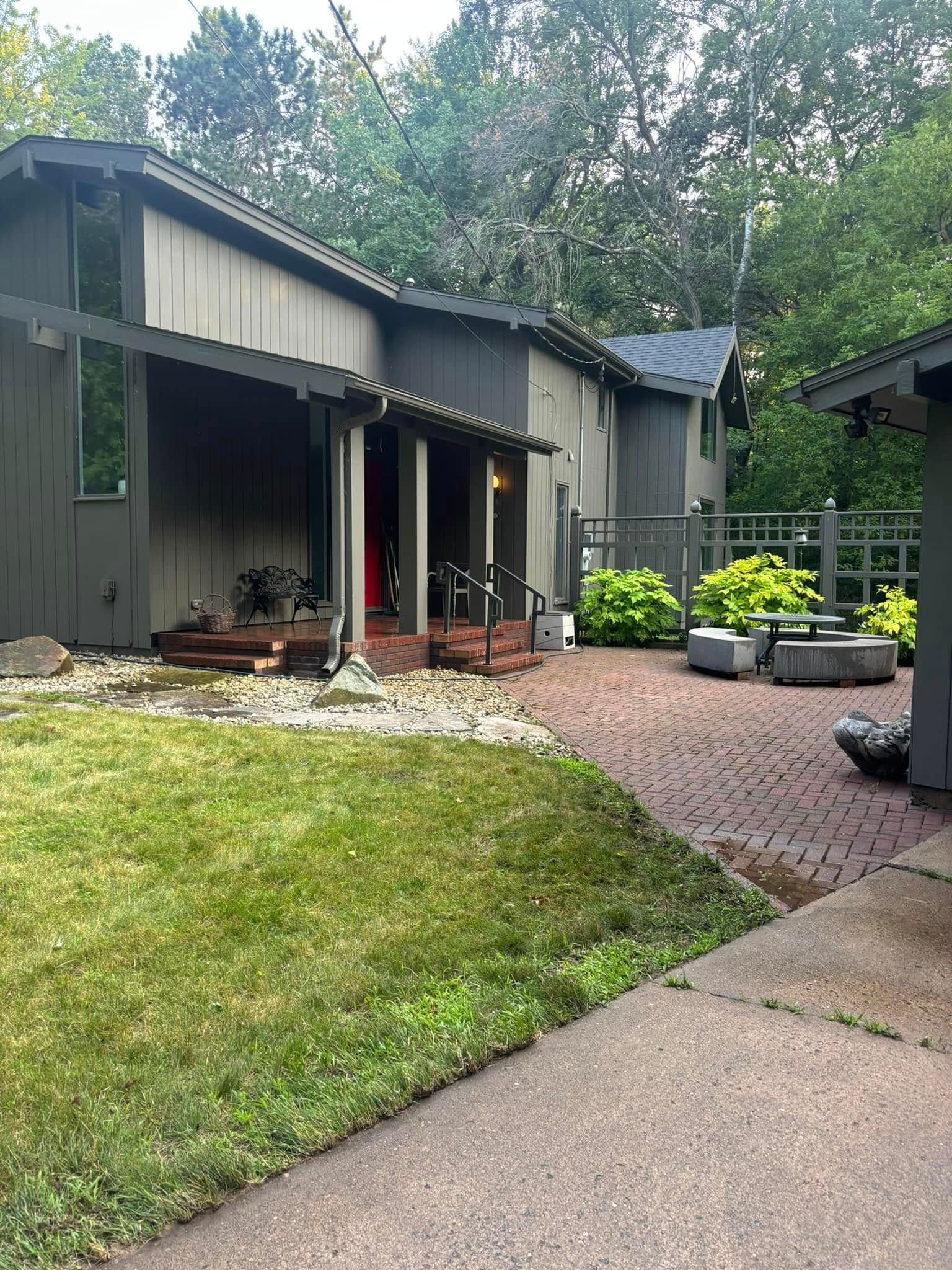 Backyard patio with gray house, gravel path, and round planters beside a green lawn