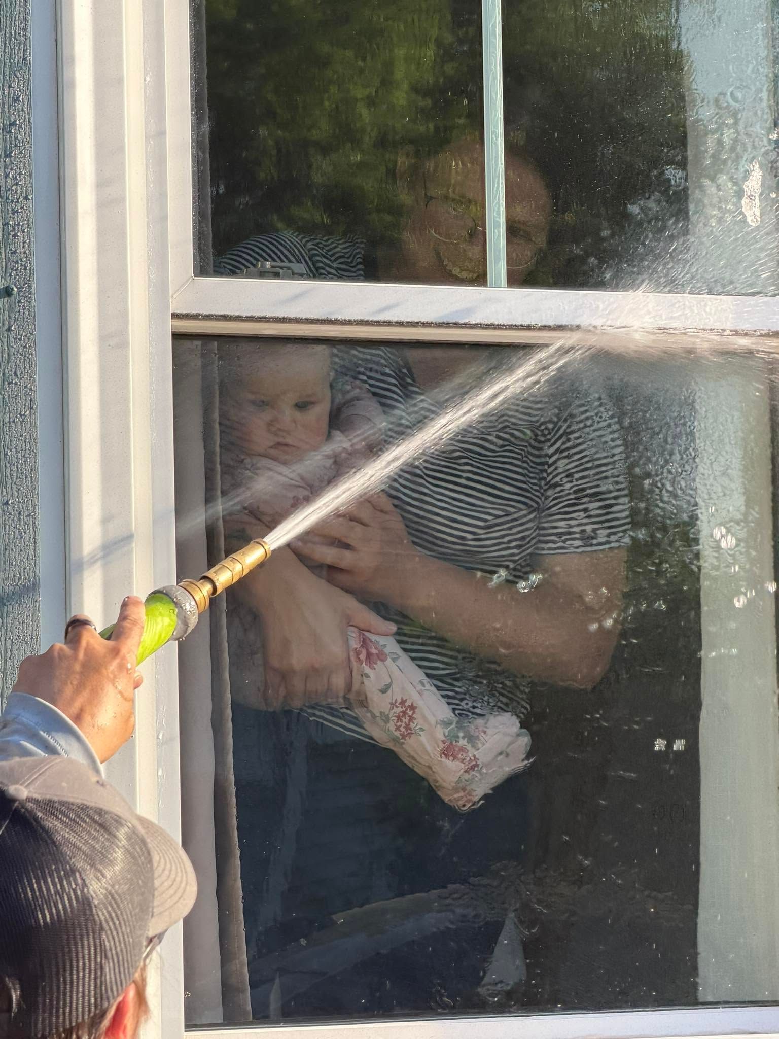 Person at a window being sprayed with water from a hose outside
