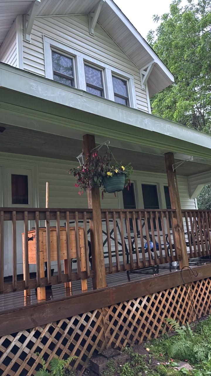 Two-story house with gray siding, green trim, and a front porch with wooden railing