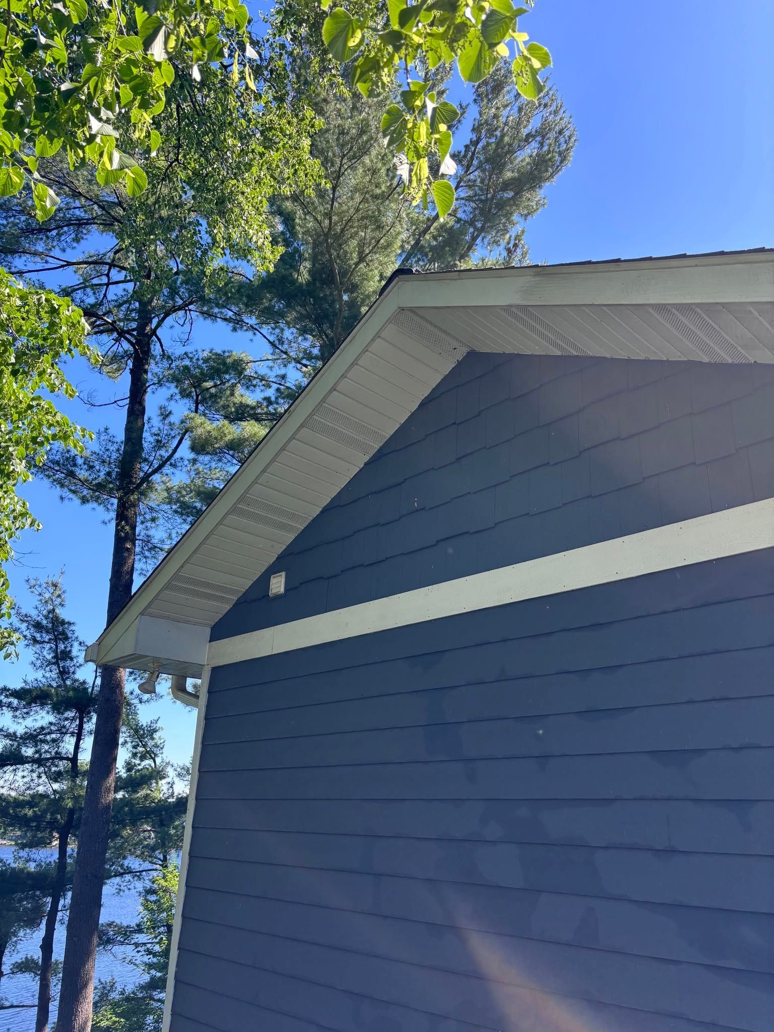 Blue house exterior with white trim and roofline against a sunny sky and tall trees