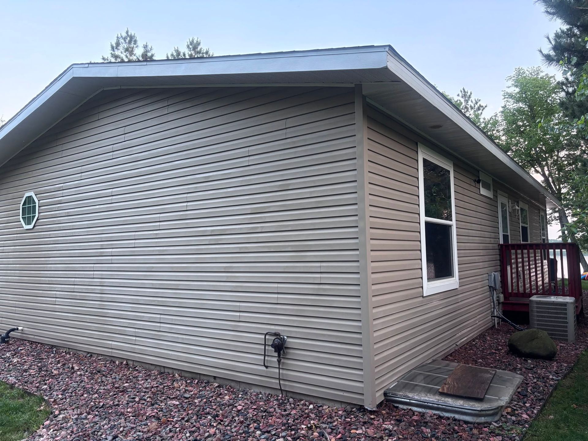 Single-story beige vinyl-sided house exterior with a side window, small porch, and gravel landscaping