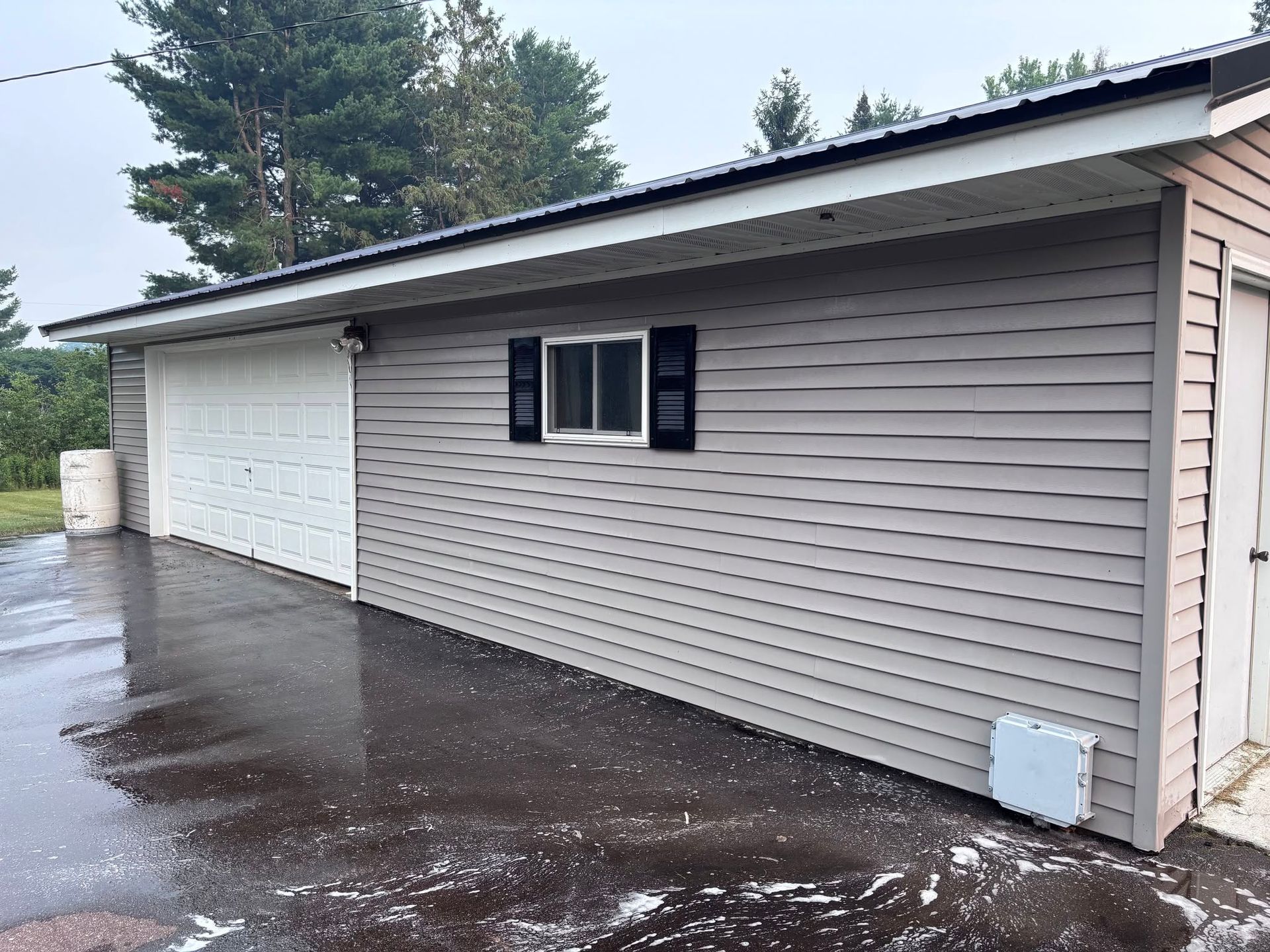 Rainy exterior of a beige garage with white doors and black-trimmed windows, seen from the driveway