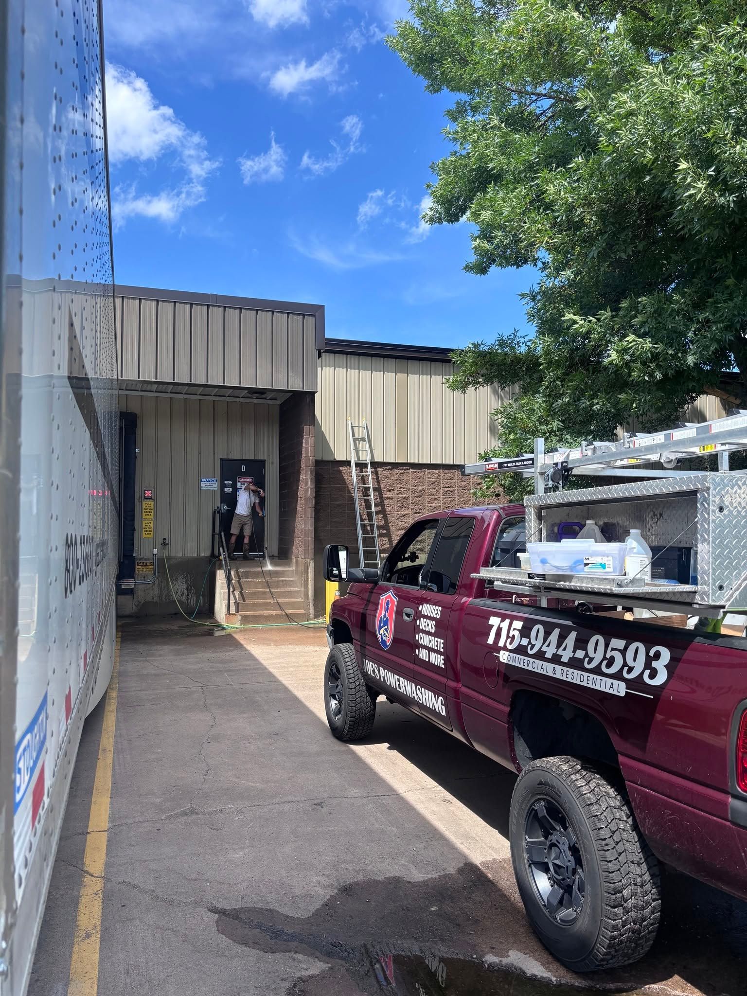 Maroon work truck parked by an industrial building under a blue sky, with trees and a loading area nearby