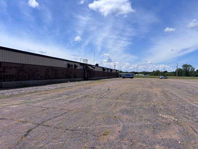 Empty gravel lot beside a long industrial building under a bright blue, partly cloudy sky