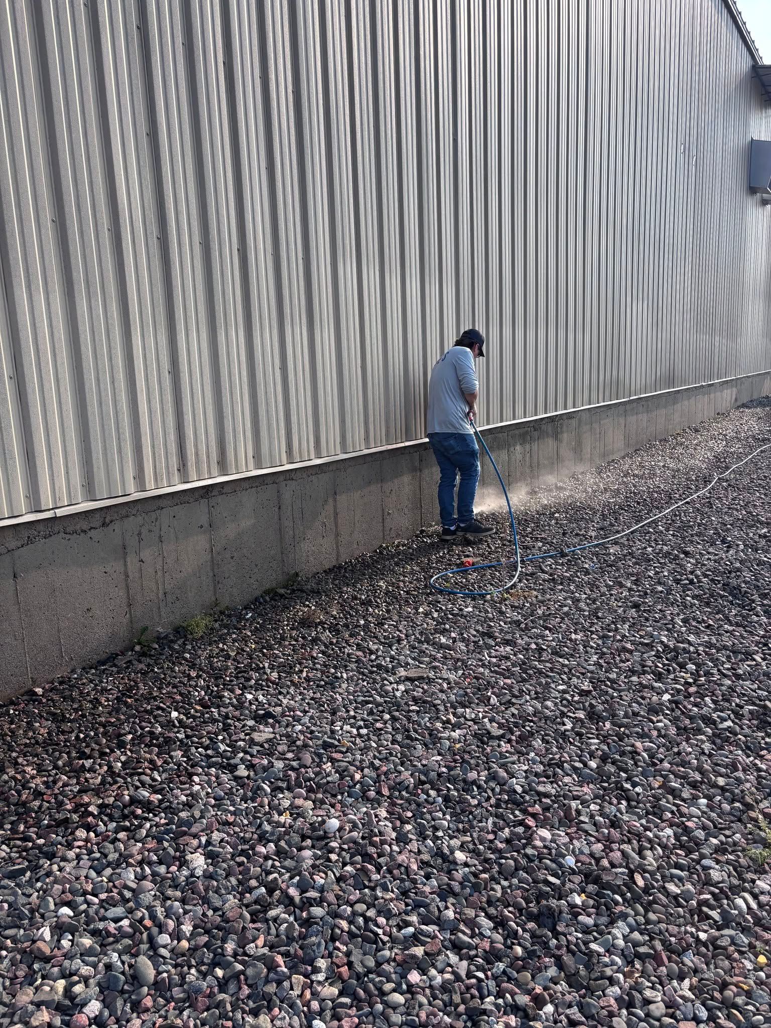 Person standing by a corrugated metal wall on a gravel-covered ground.