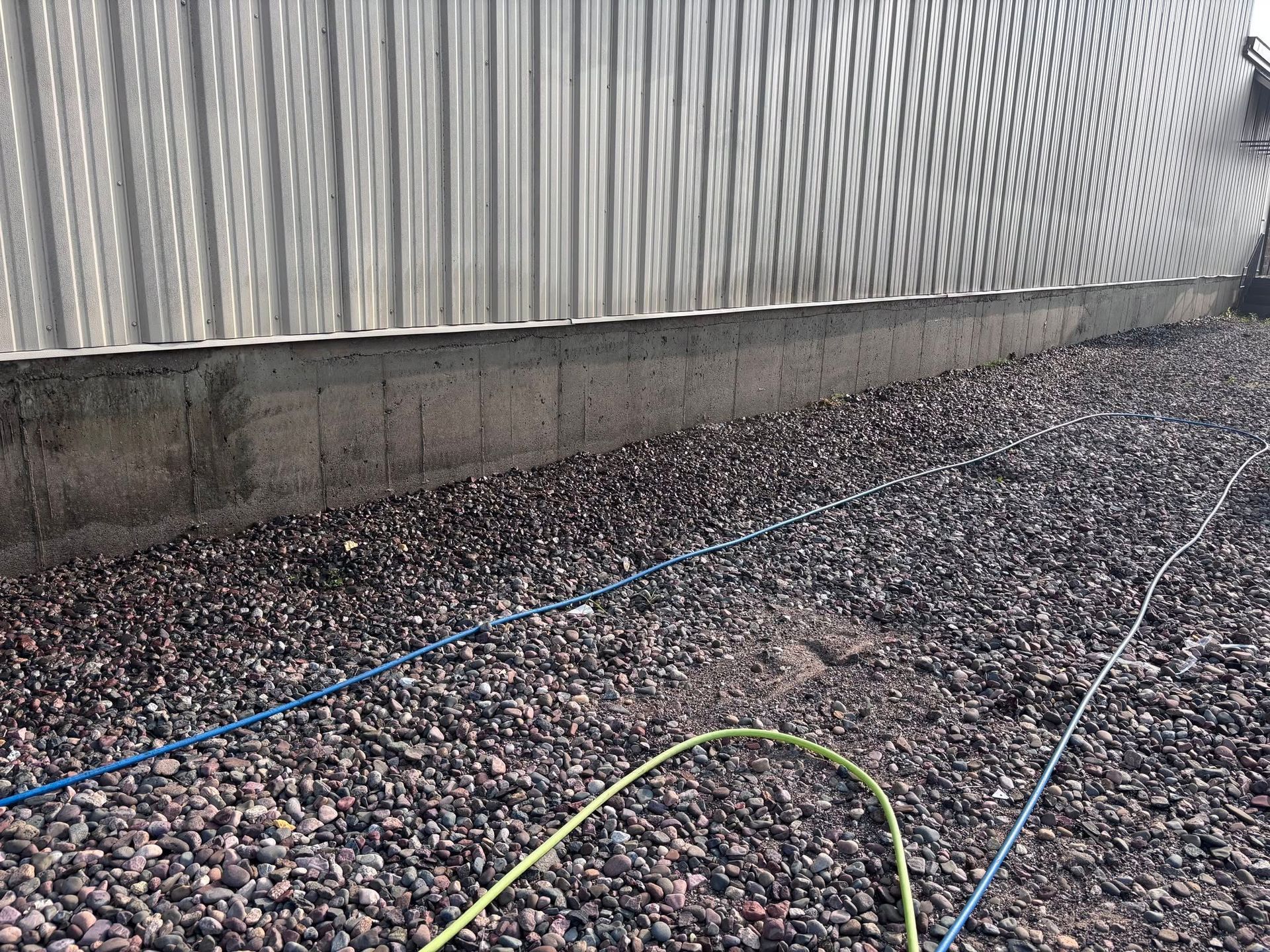 Blue and green hoses on gravel beside a corrugated metal wall