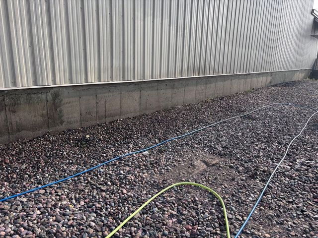 Blue and green hoses on gravel beside a corrugated metal wall