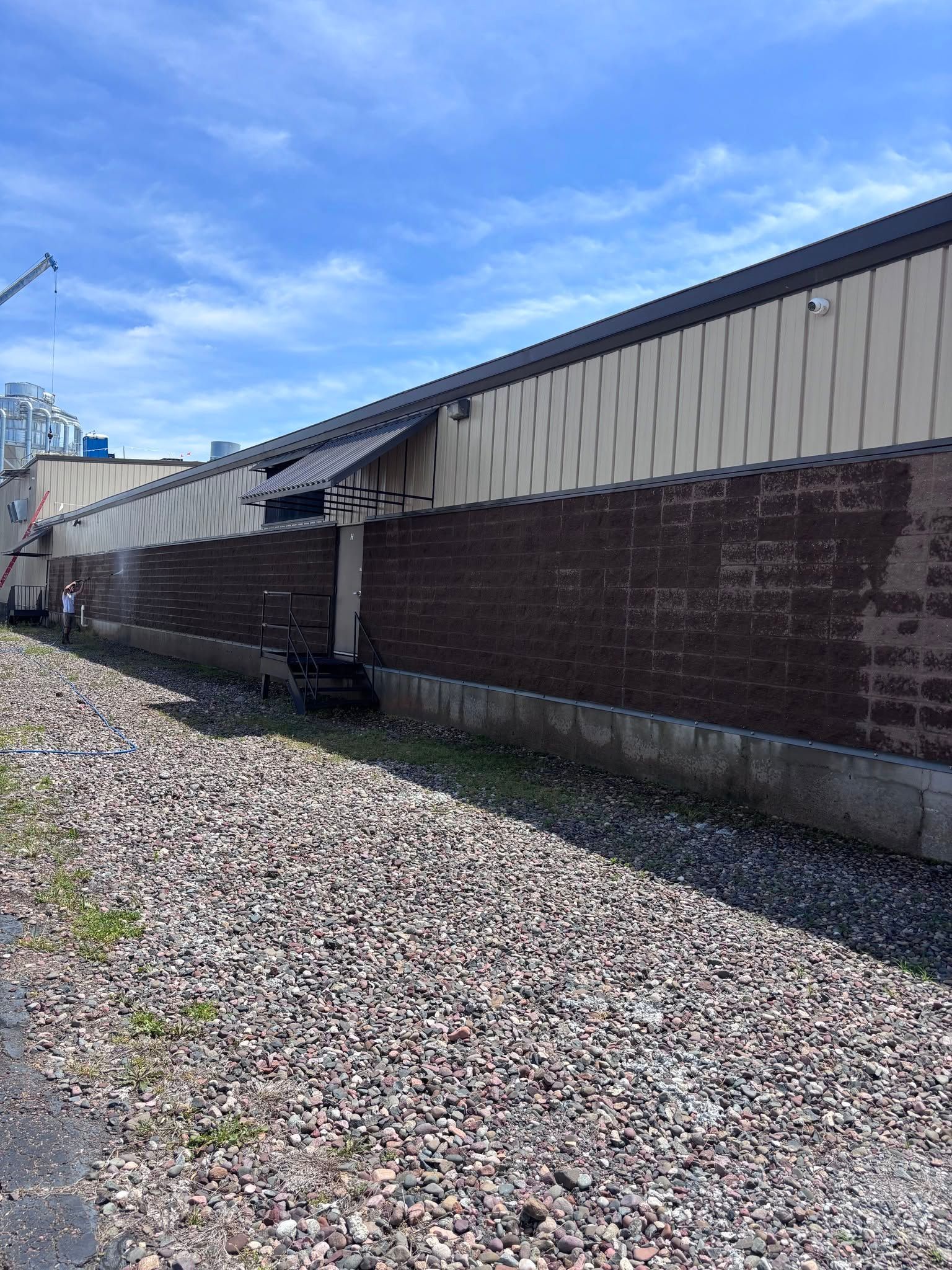 Long brick industrial building beside a gravel yard under a blue sky