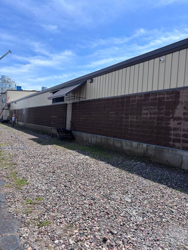 Long brick industrial building beside a gravel yard under a blue sky
