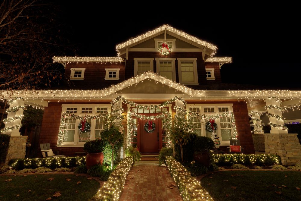 House covered in warm white Christmas lights, with wreaths and a lit front door at night
