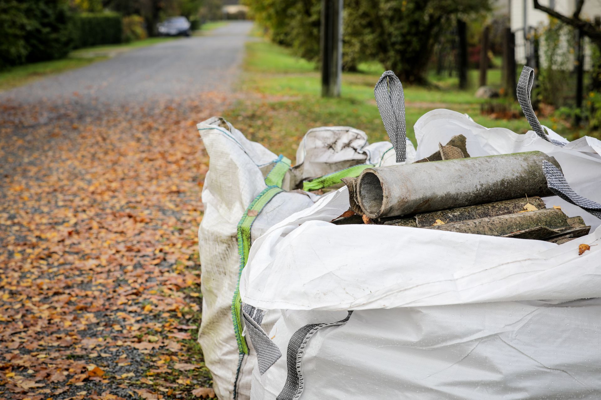 Asbestos waste pipes and roofing sheets in white bags on a leaf-filled road. Asbestos waste pipes and roofing sheets in white bags on a leaf-filled road.