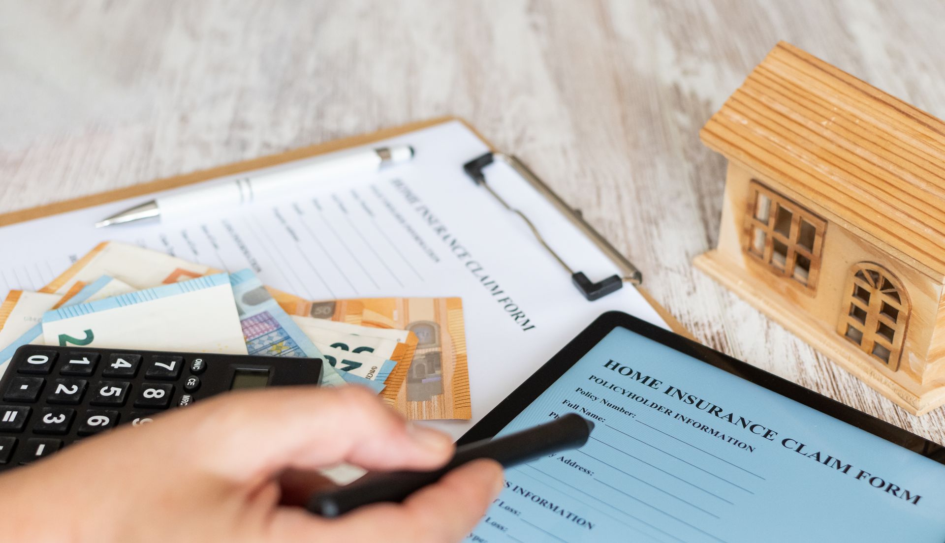 Home insurance claim form with calculator, cash, and model house on a desk.
