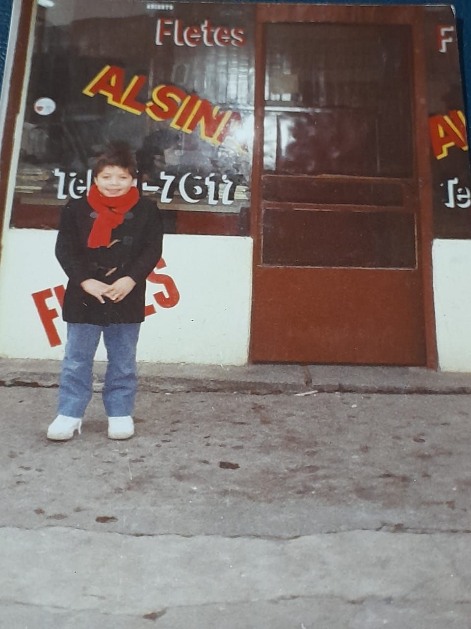 Una persona está de pie en la acera frente a una tienda con letreros pintados y una puerta marrón.