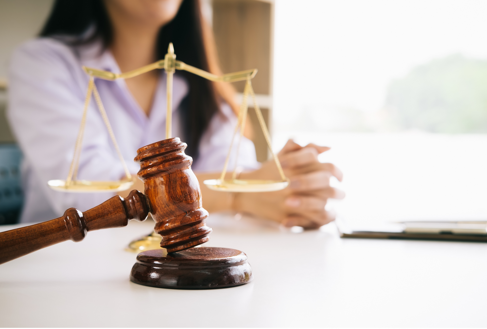 Gavel and scales of justice on a desk with a blurred person writing in the background