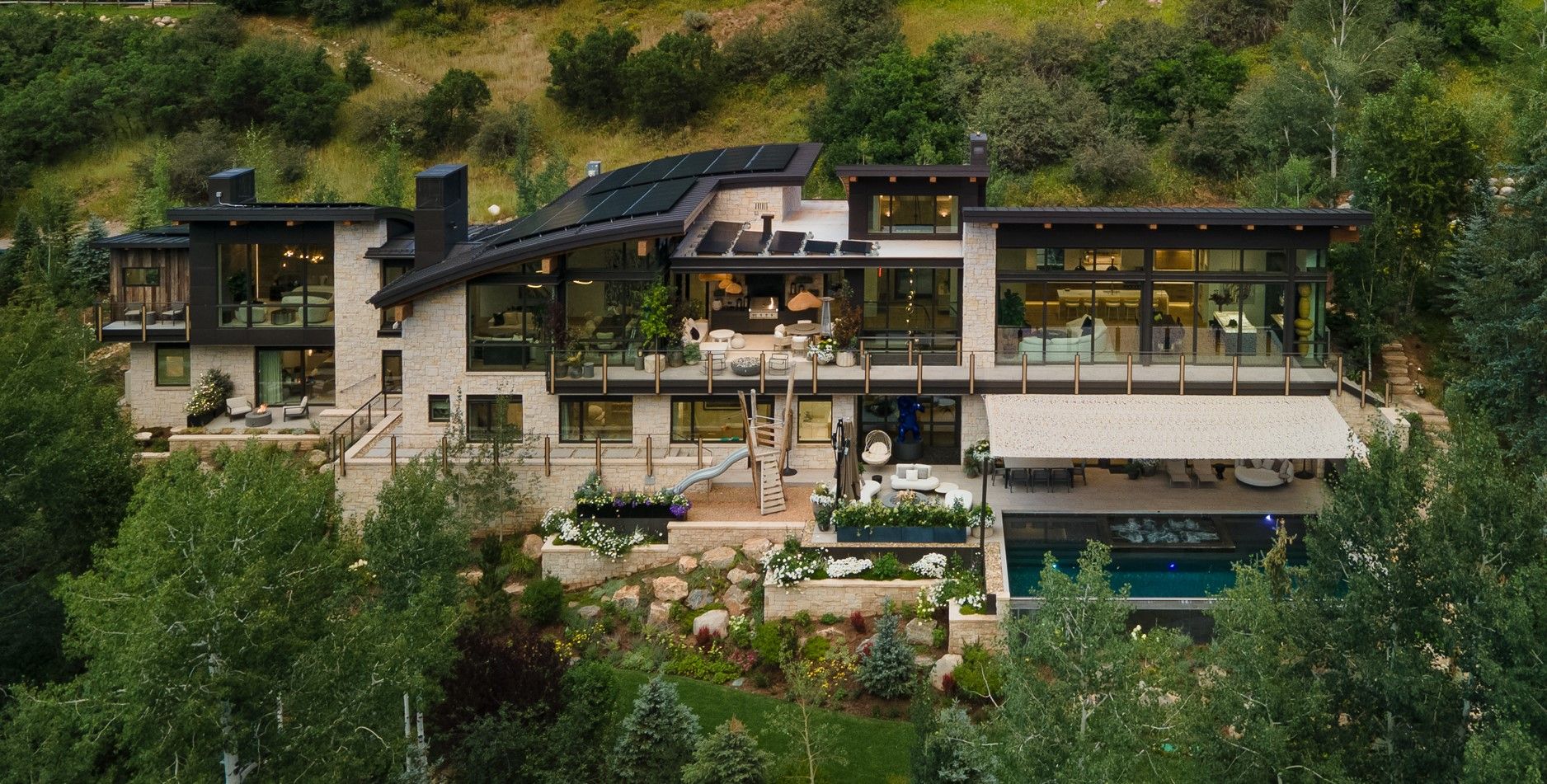A large house is sitting on top of a hill surrounded by trees and mountains.