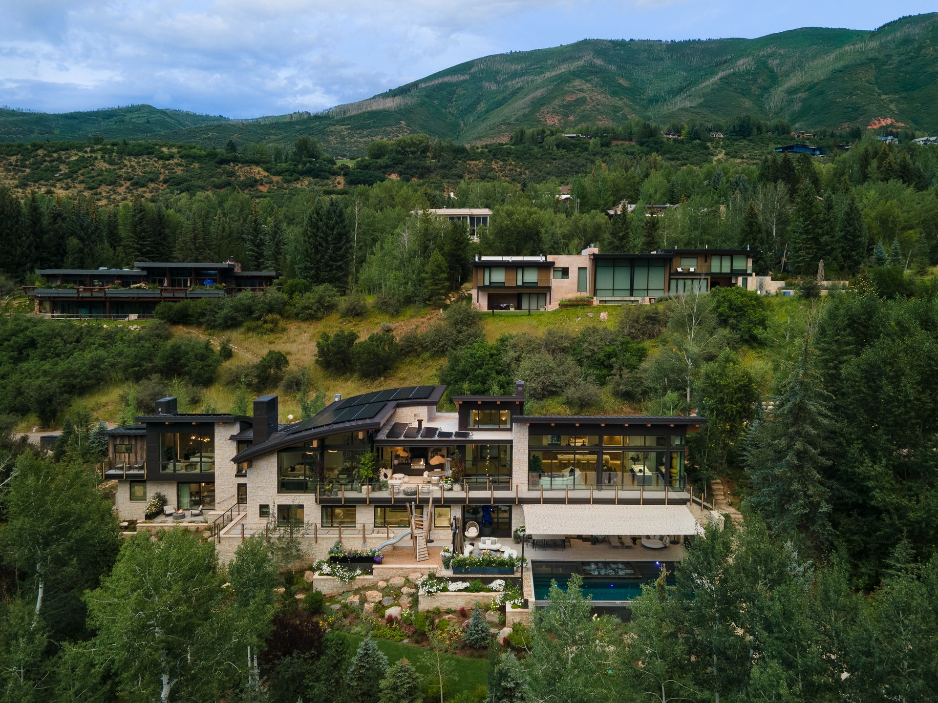 A large house is sitting on top of a hill surrounded by trees and mountains.