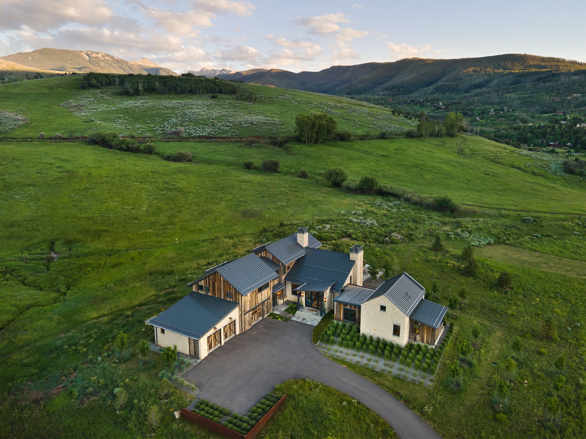 An aerial view of a house in the middle of a grassy field with mountains in the background.