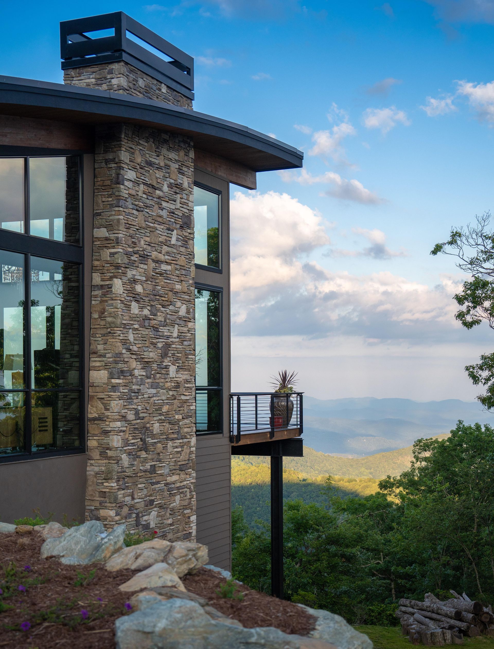 A house with a large stone chimney and a balcony overlooking a mountain.