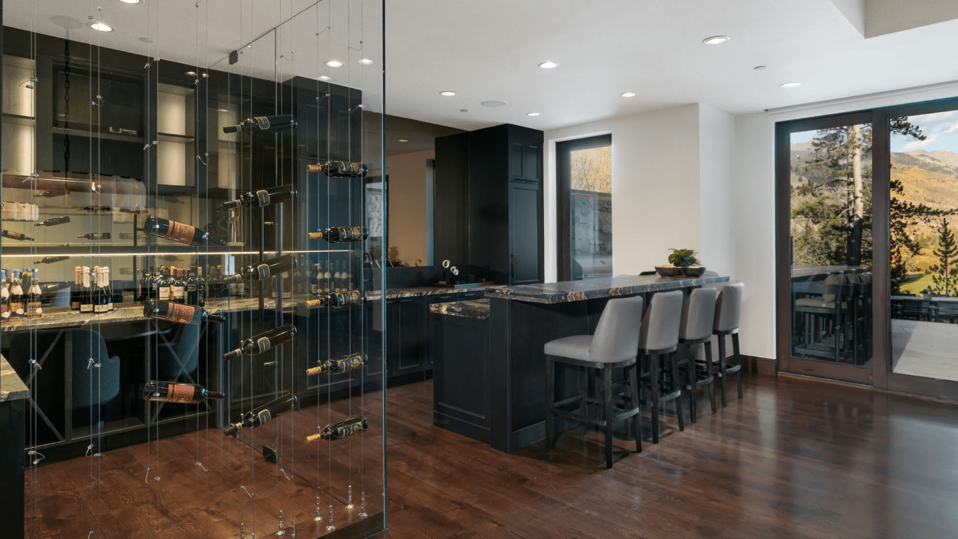 A kitchen with a bar and a wine cellar behind a glass wall.
