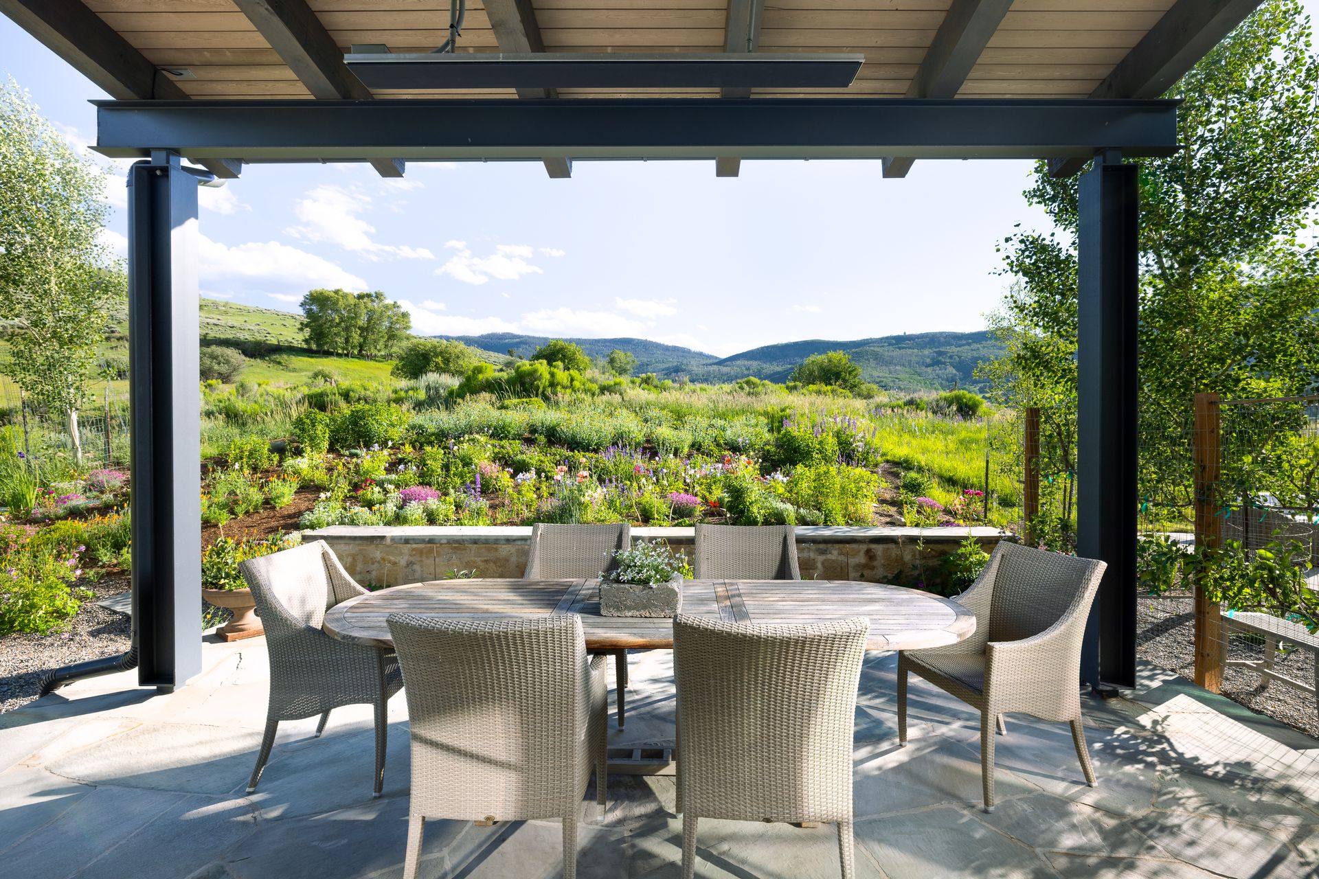 An aerial view of a house in the middle of a grassy field with mountains in the background.