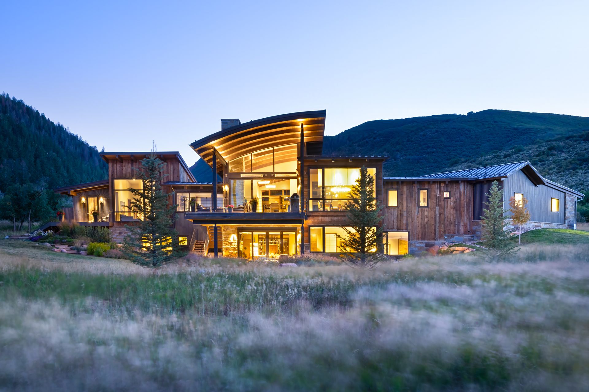 A large house is sitting in the middle of a field with mountains in the background.