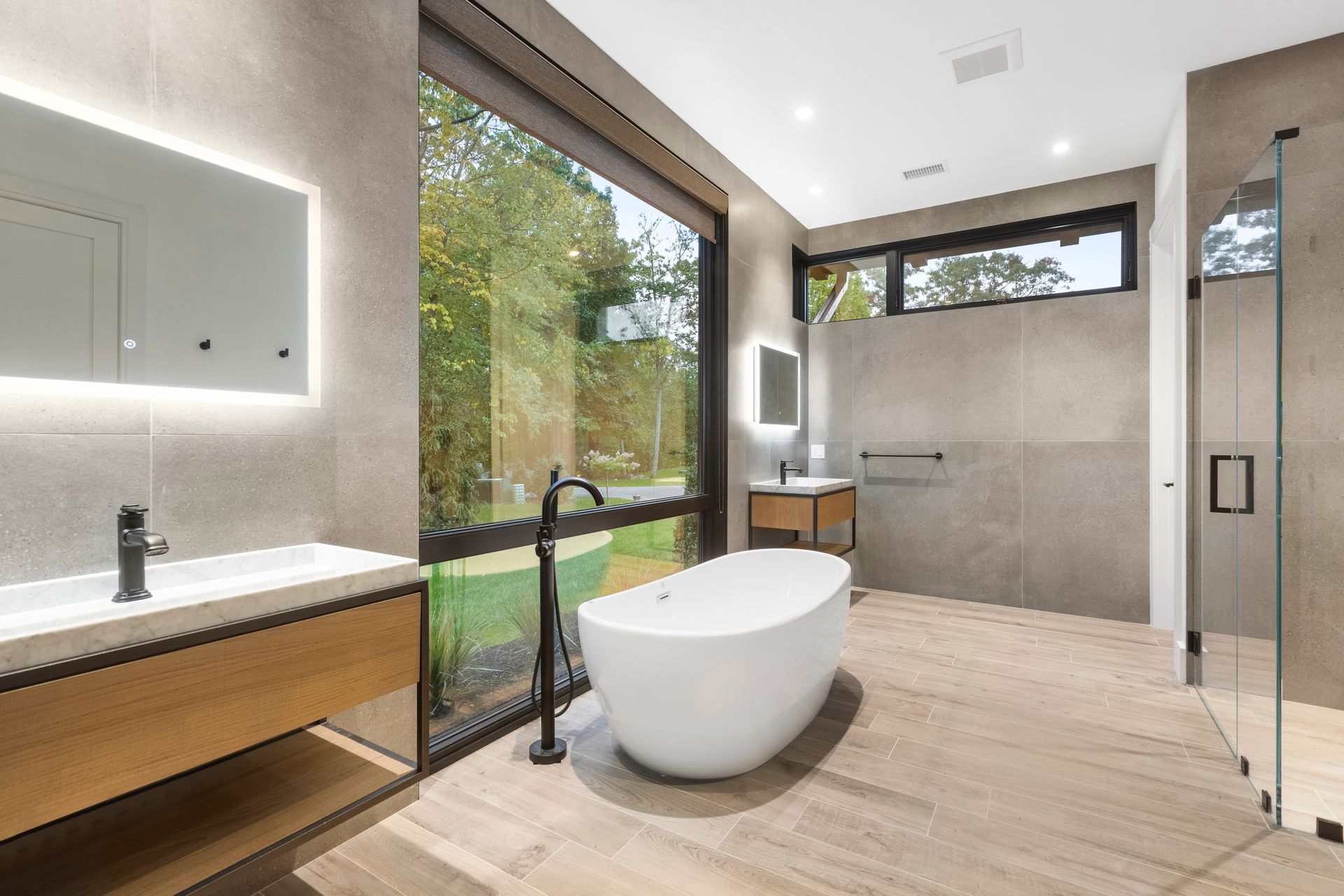 A bathroom with a tub , sink , mirror and large window.
