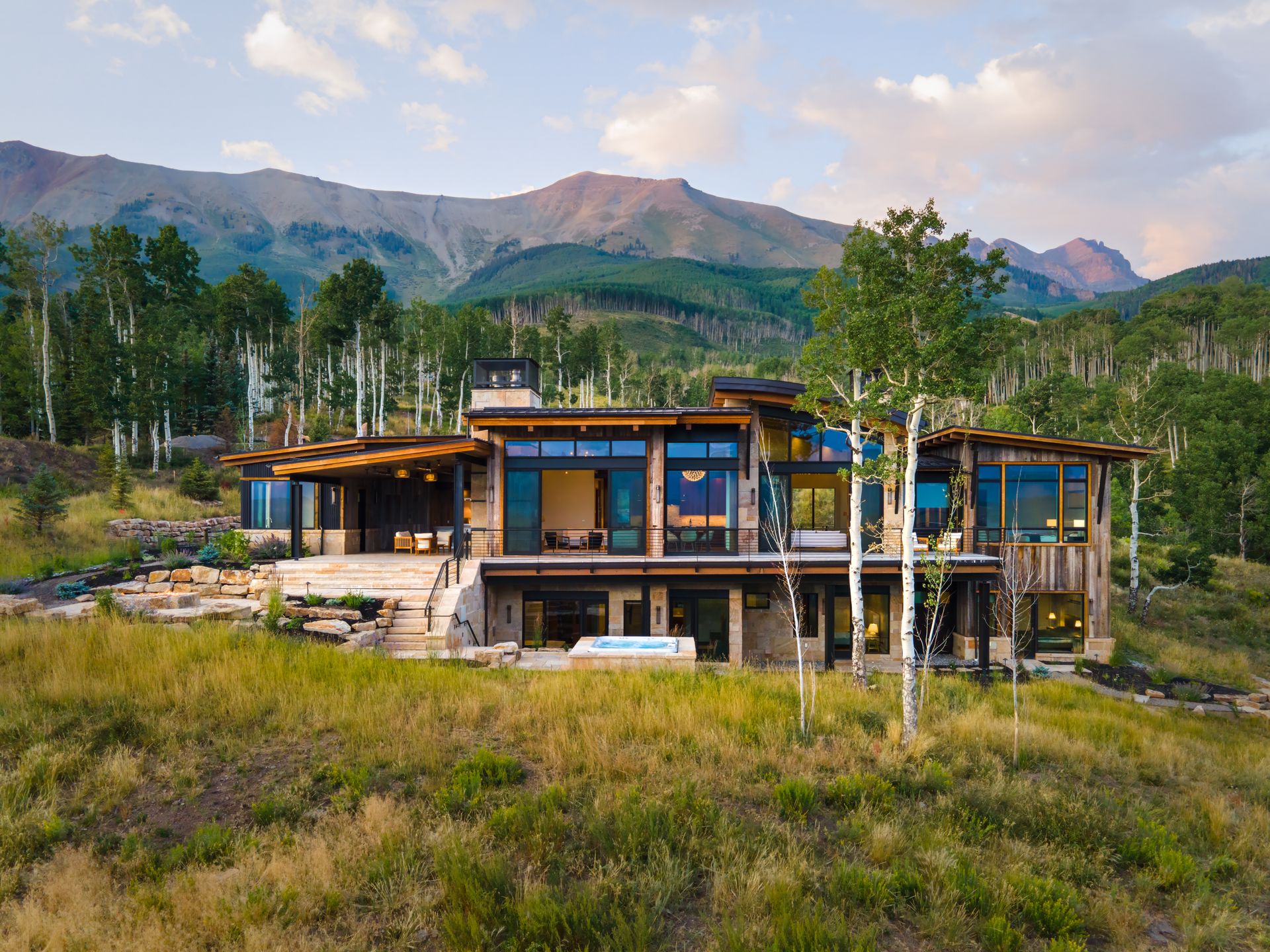 A large house is sitting on top of a grassy hill with mountains in the background.