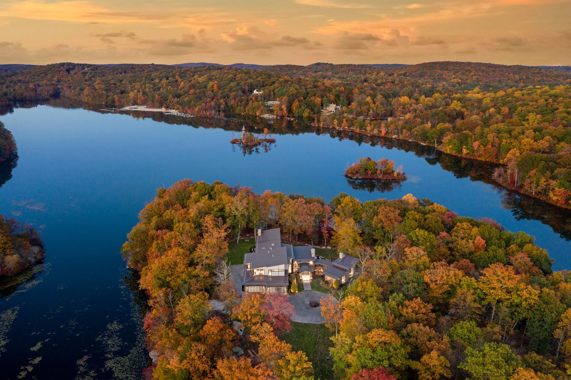 An aerial view of a house on a small island in the middle of a lake surrounded by trees.
