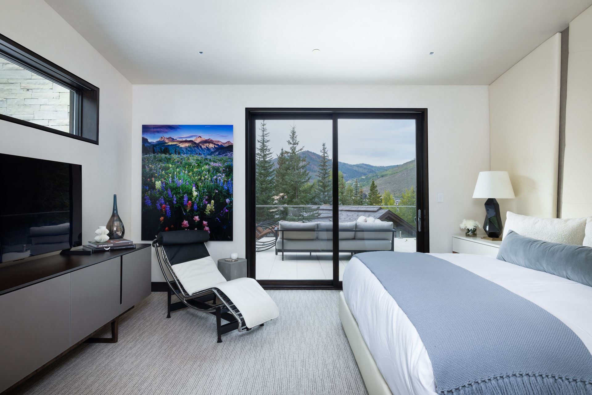 A bedroom with a large bed , television , chair and sliding glass doors.