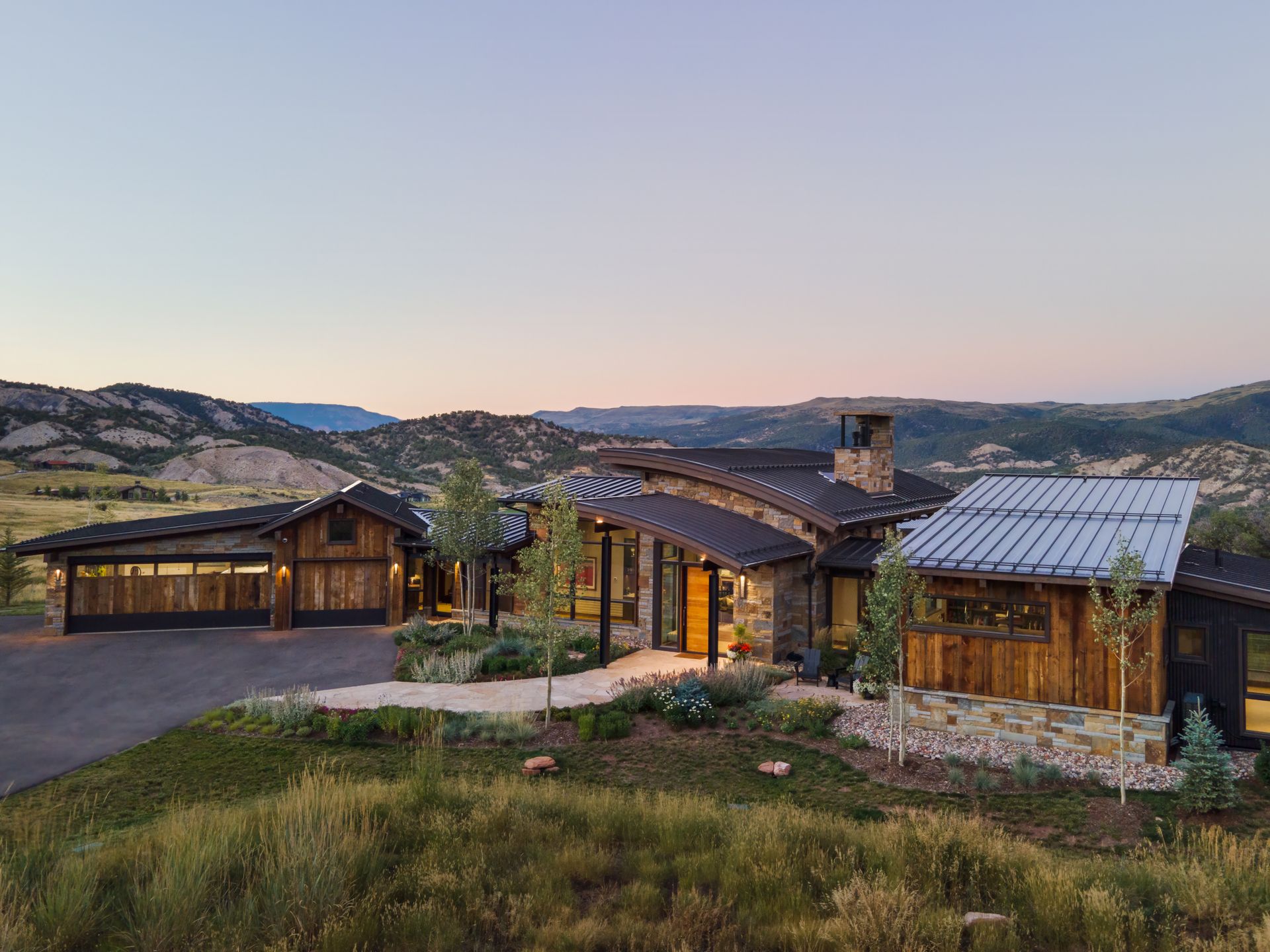 An aerial view of a large house in the middle of a field with mountains in the background.