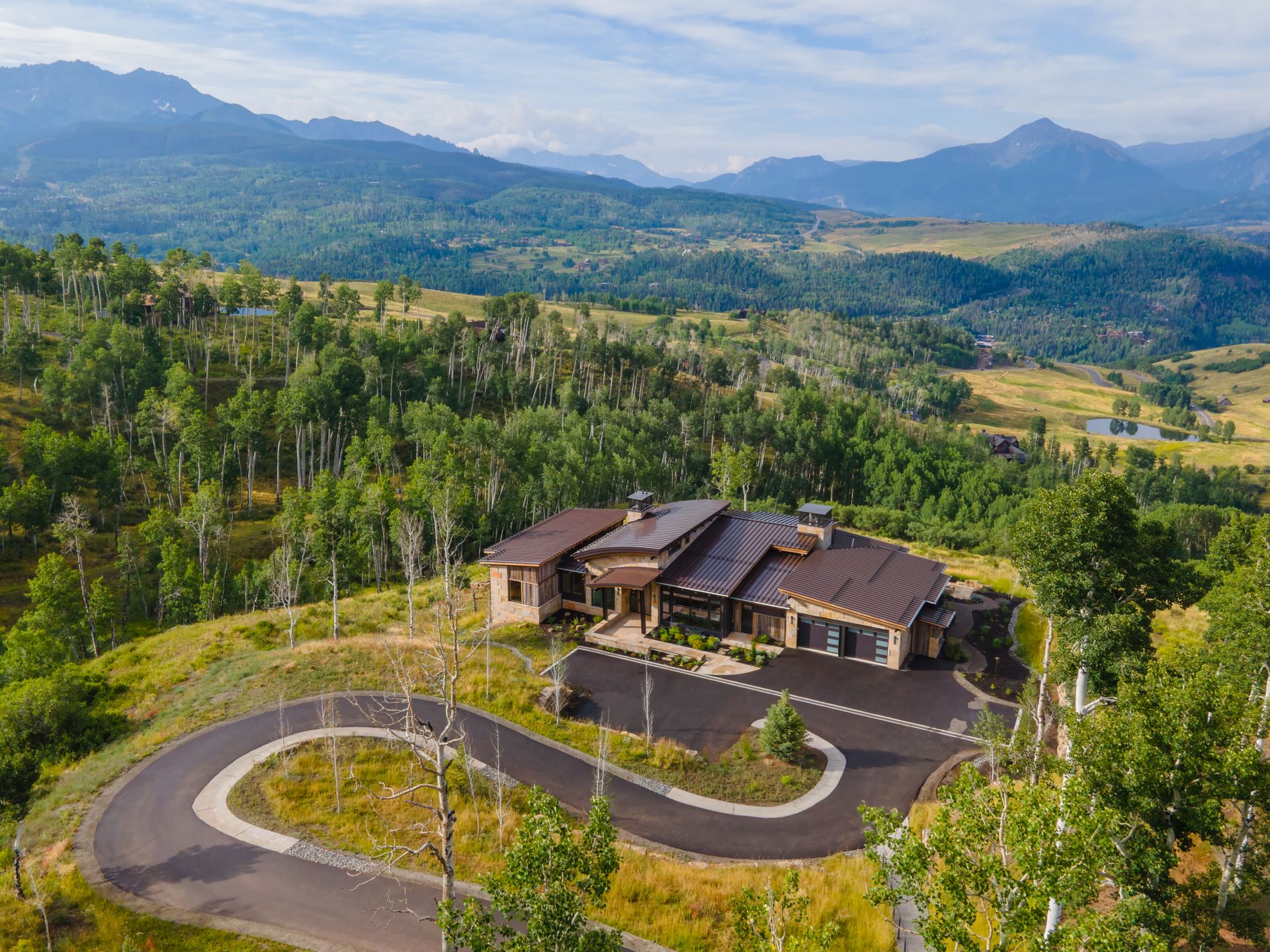 An aerial view of a house on top of a hill with mountains in the background.