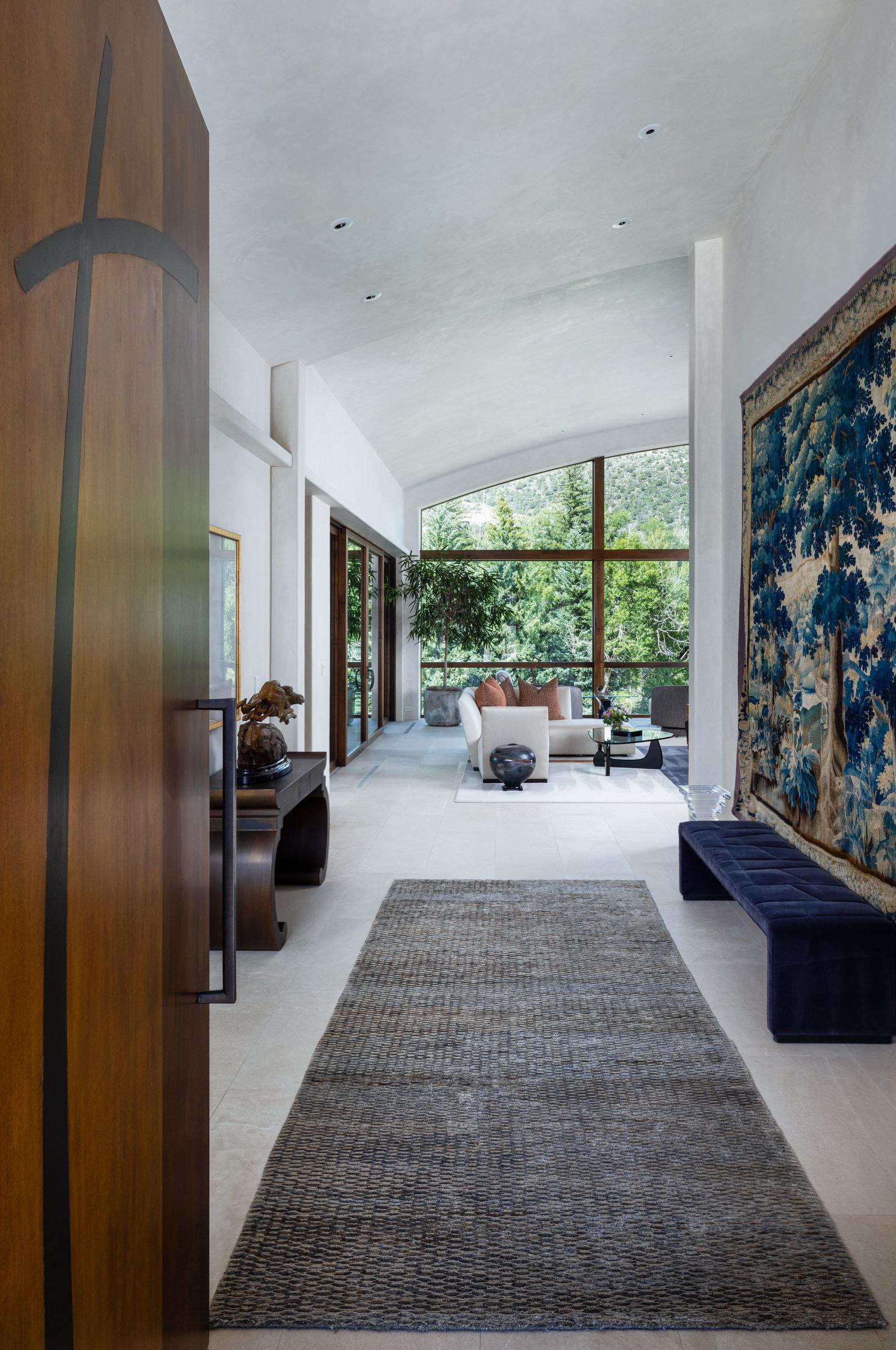A hallway in a house with a rug and a large window.