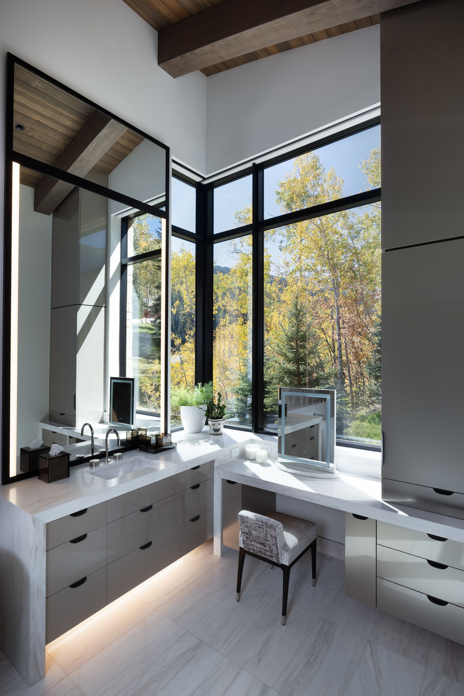 A bathroom with a vanity , mirror and large windows.