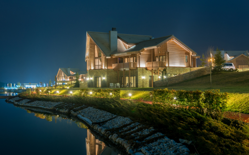 A large house is sitting on the shore of a lake at night.