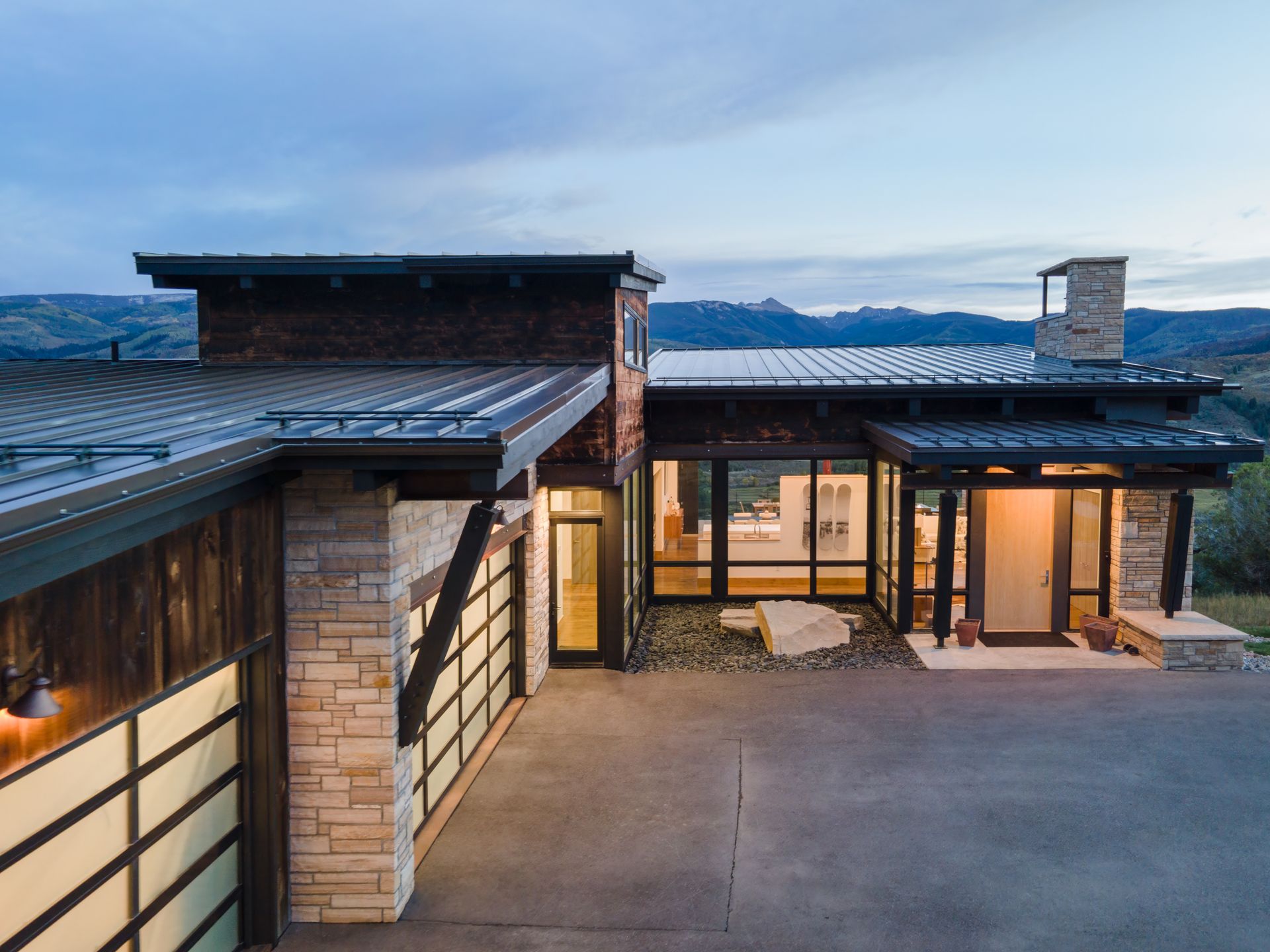 An aerial view of a modern house with a large garage and mountains in the background.