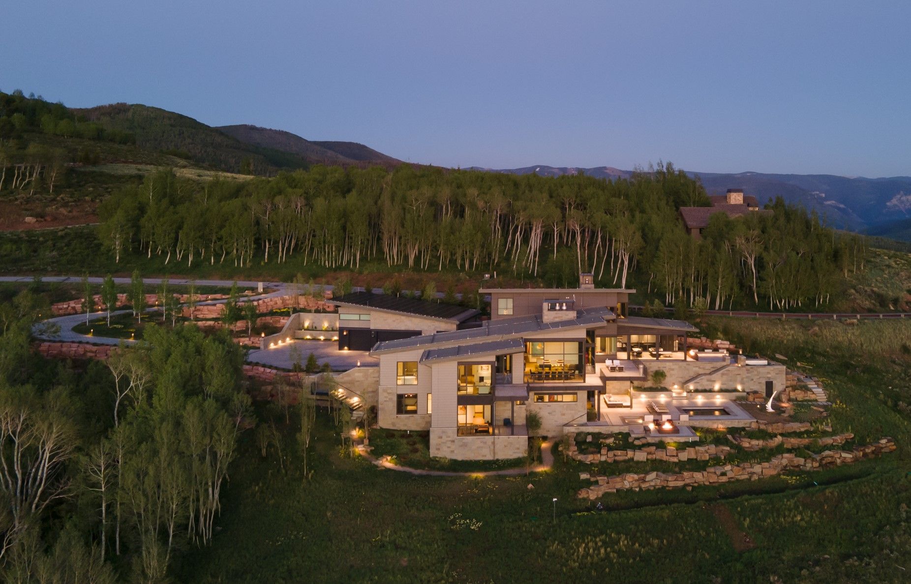 A large house is sitting on top of a hill with a driveway leading to it.
