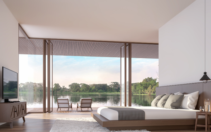 A bedroom with a large bed , television , and balcony overlooking a lake.