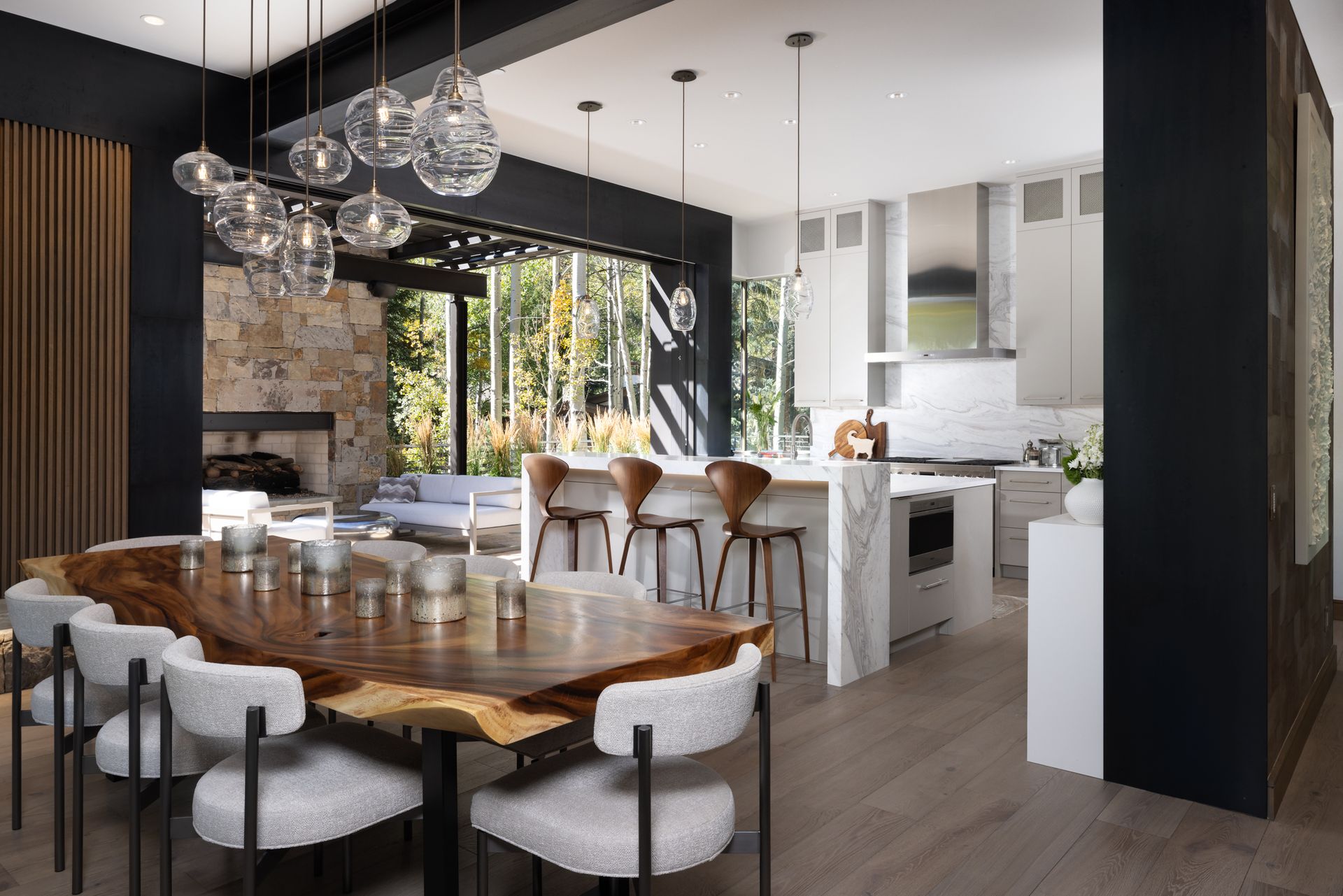 A dining room with a wooden table and chairs and a kitchen in the background.