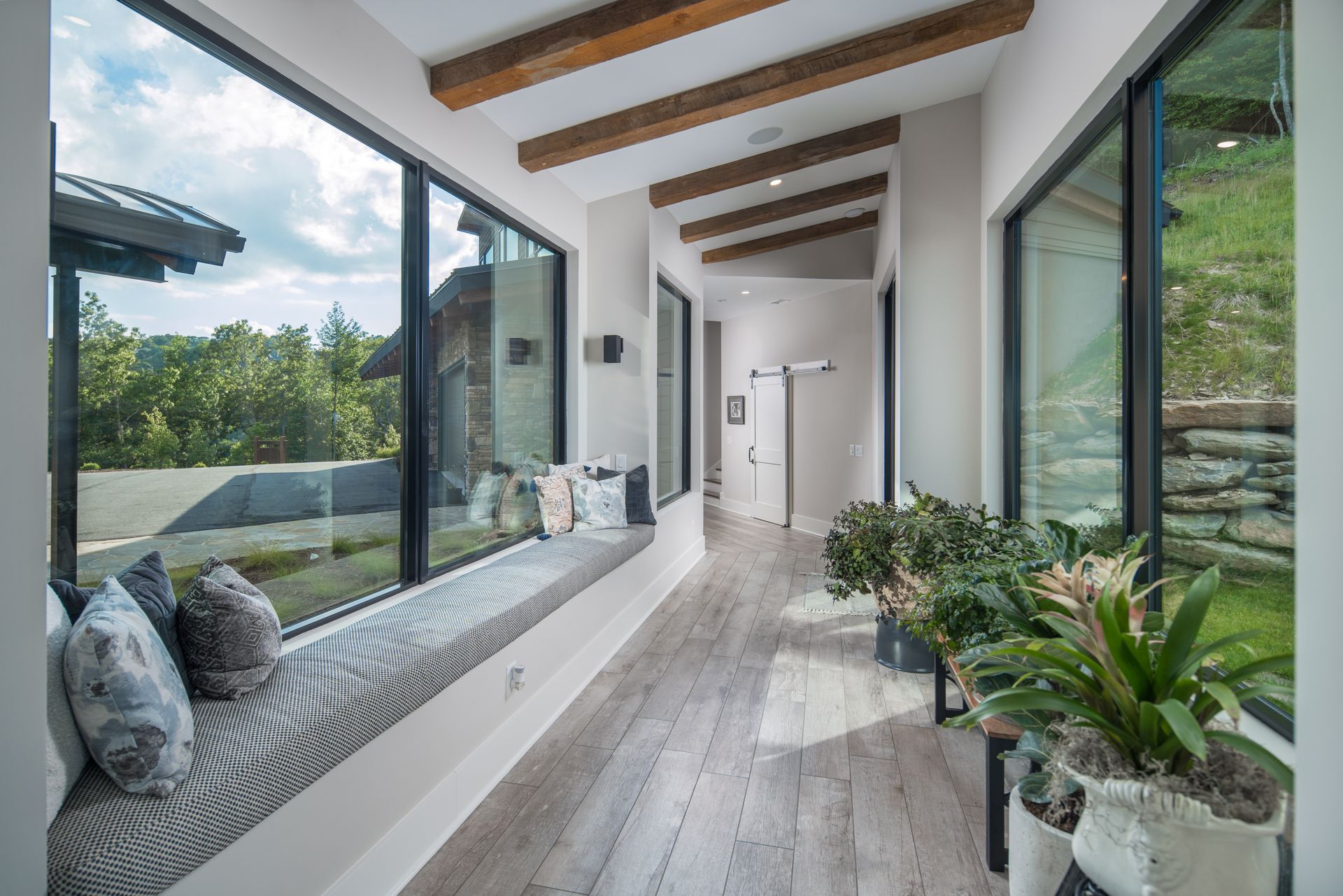 A long hallway with a window seat and potted plants.