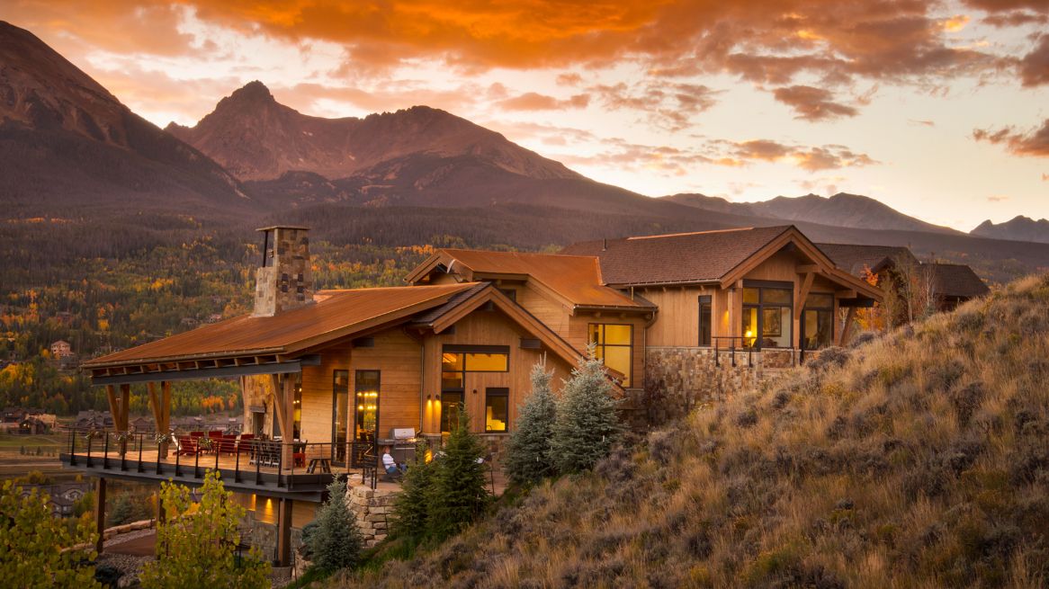 A large house is sitting on top of a hill with mountains in the background.