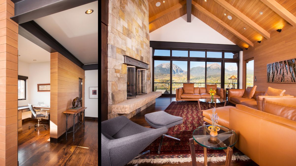 A large wooden house is sitting on top of a hill with mountains in the background.