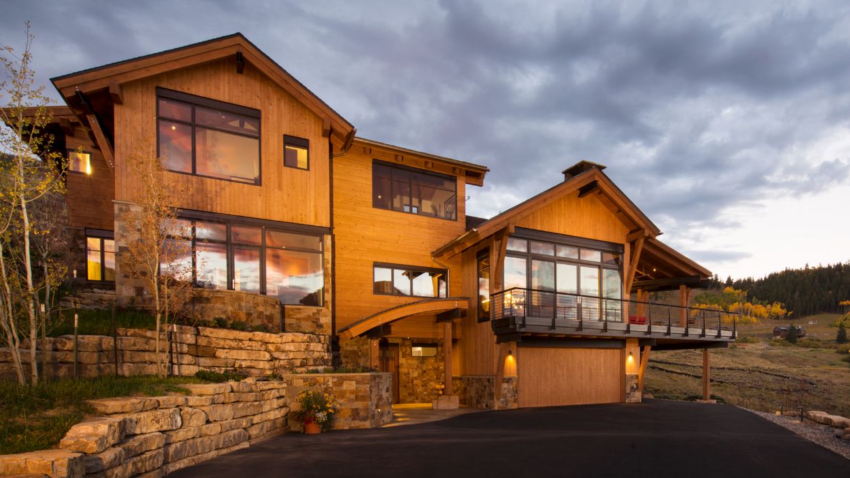 A large wooden house with a lot of windows is sitting on top of a hill.