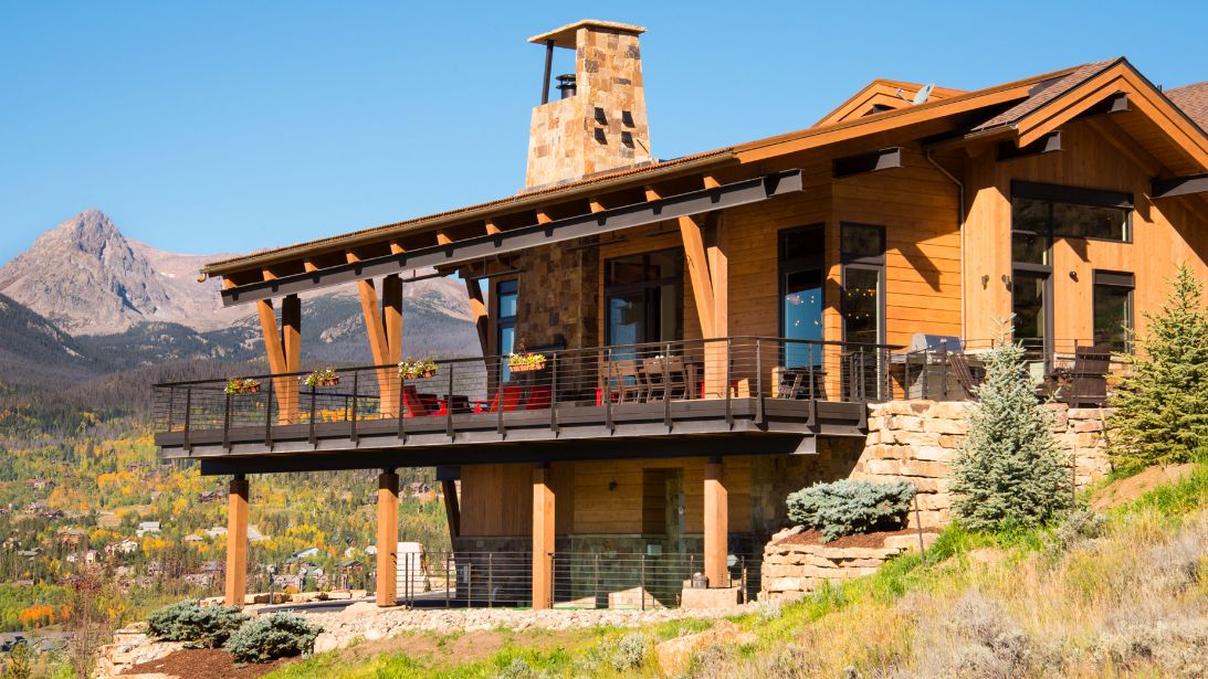 A large house is sitting on top of a hill with mountains in the background.