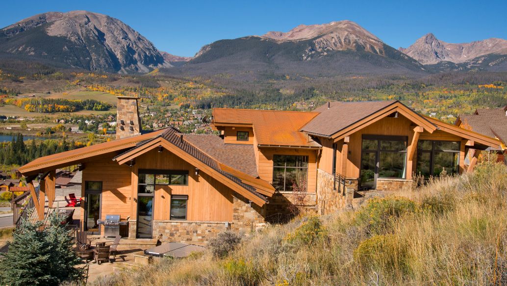 A large house is sitting on top of a hill with mountains in the background.