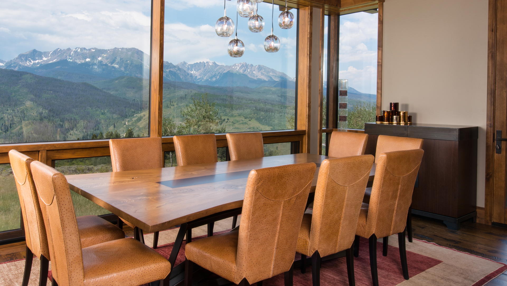 A dining room with a table and chairs and a view of the mountains.