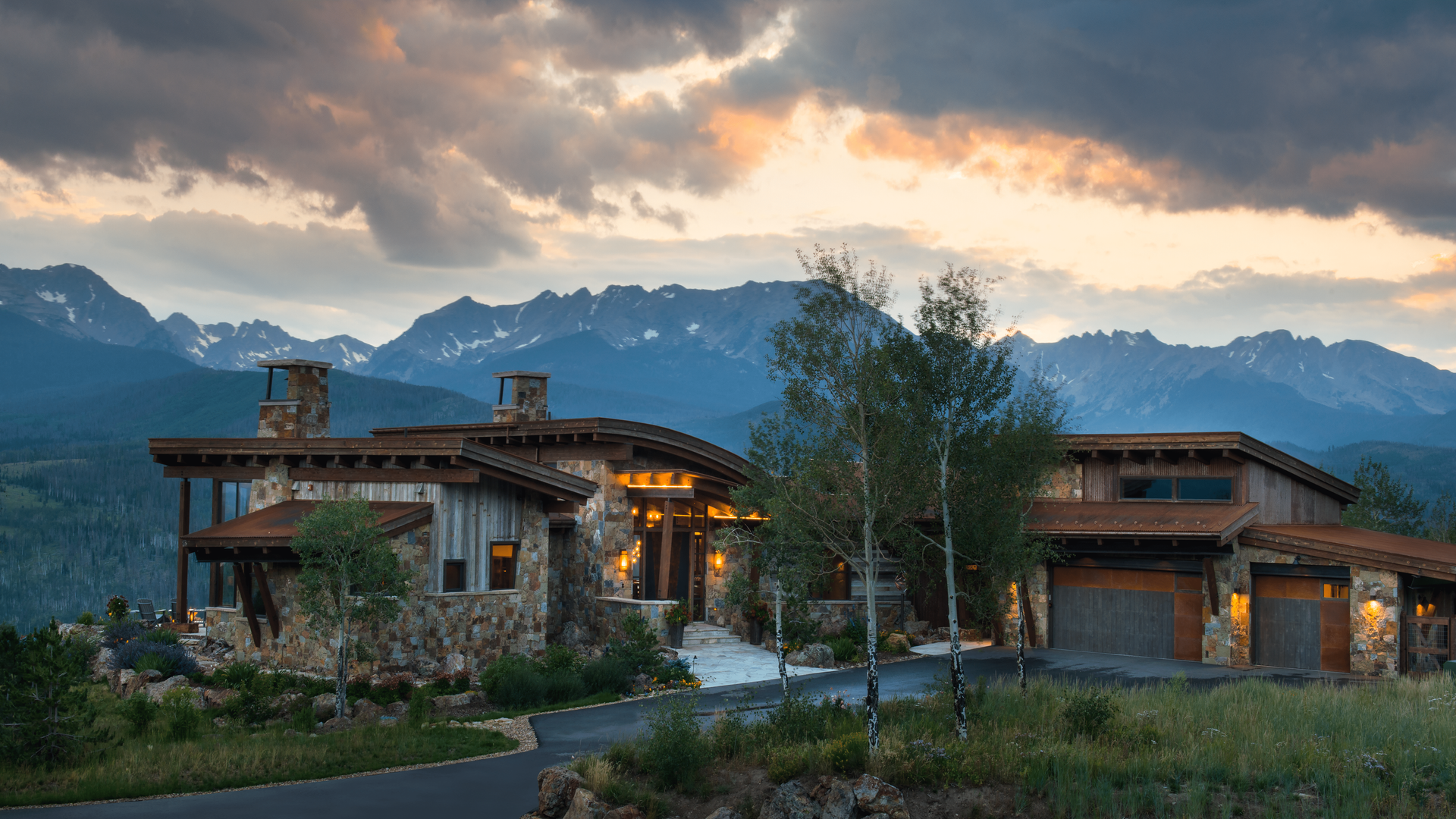 A large house is sitting on top of a hill with mountains in the background.