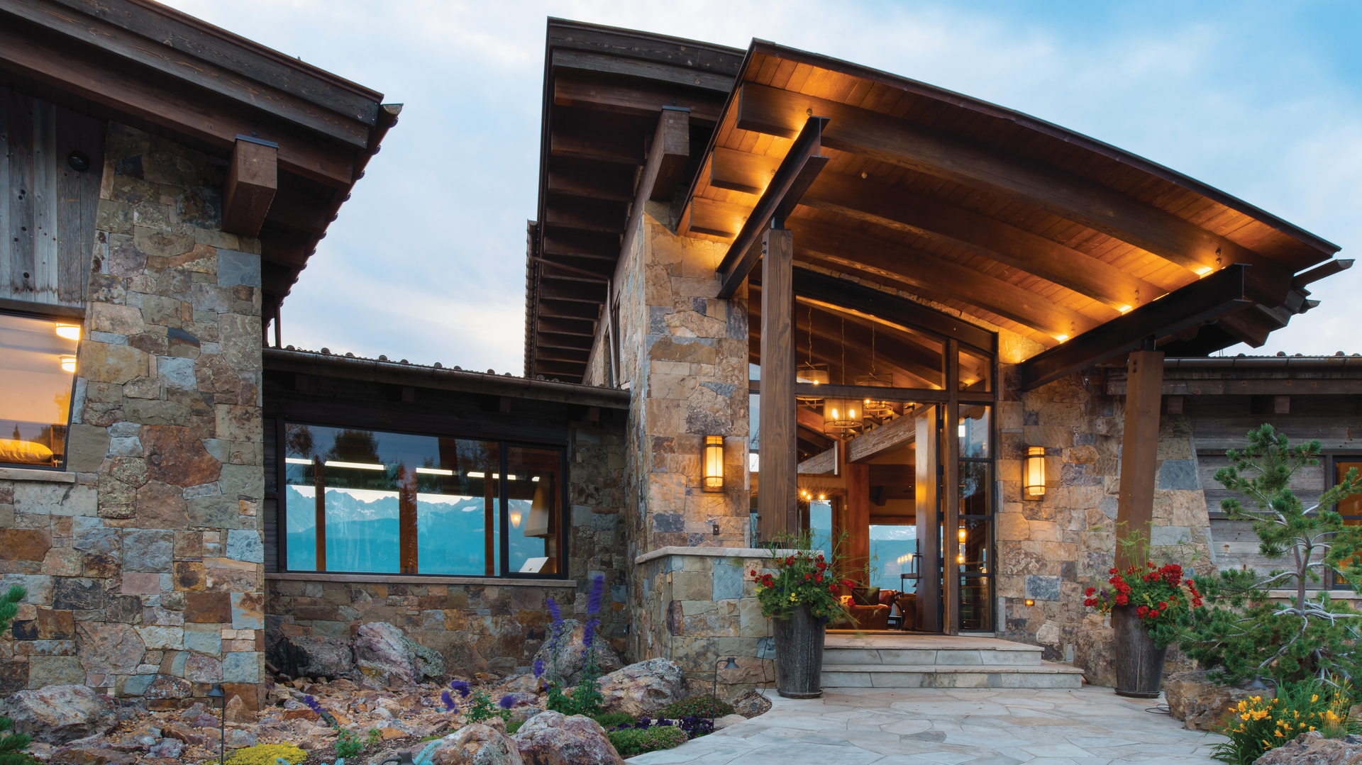 A large house is sitting on top of a grassy hill with mountains in the background.