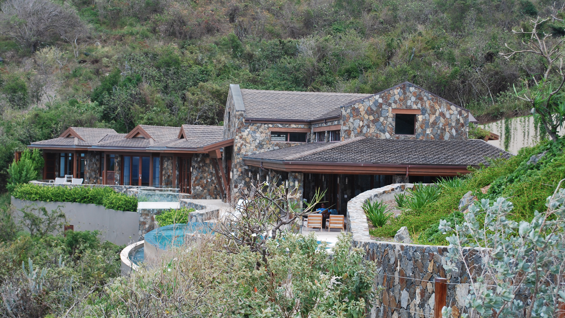 A large stone house is surrounded by trees and bushes